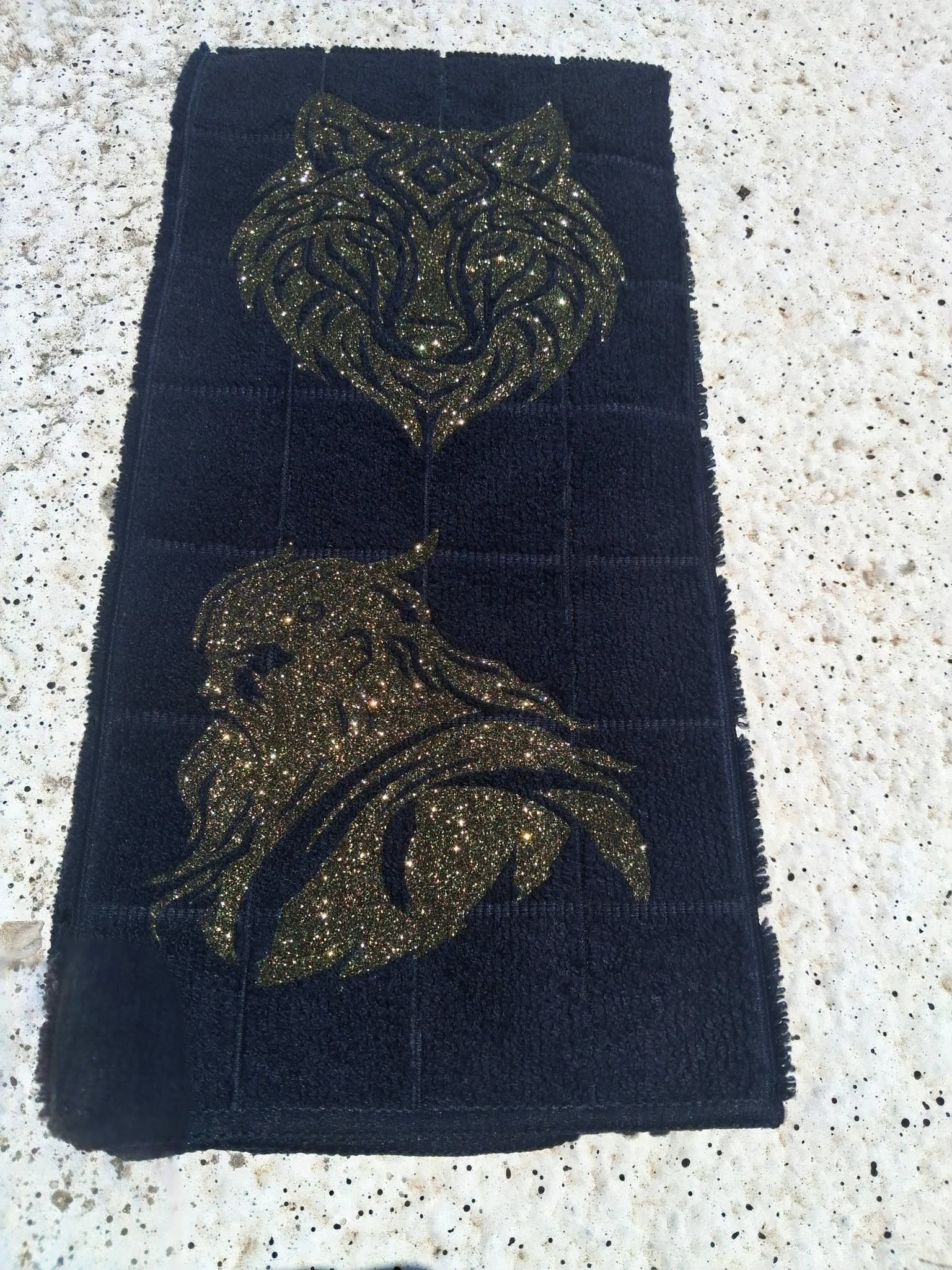 Black microfiber wolf and Viking warrior hand towel angled view on concrete showing full gold glitter design