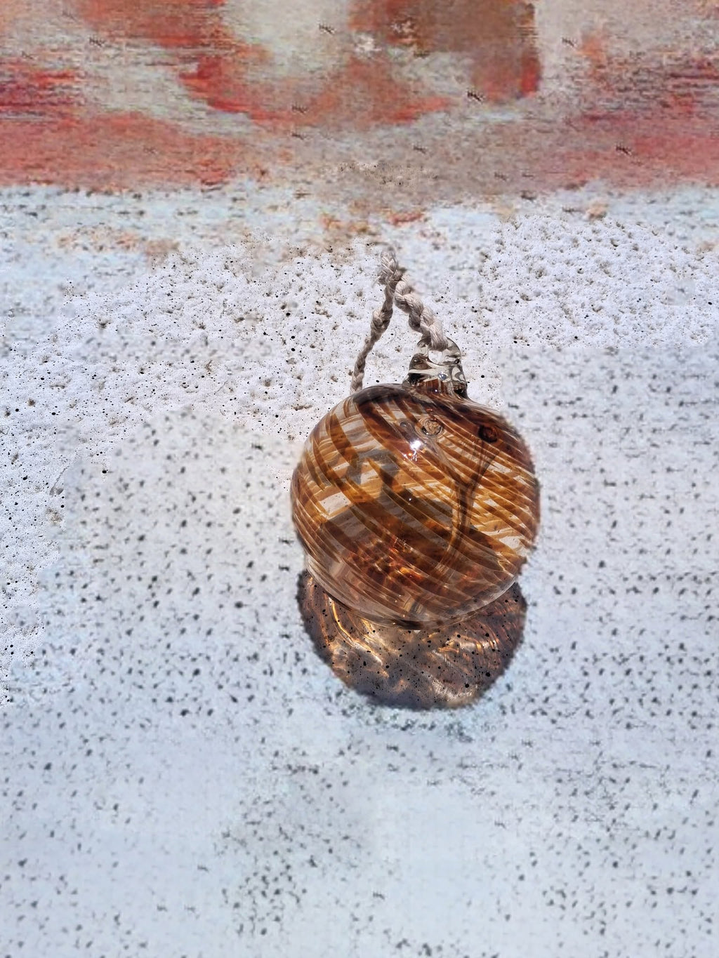 Amber swirl witch ball with braided rope hanger laying on concrete surface full view showing warm honey tones
