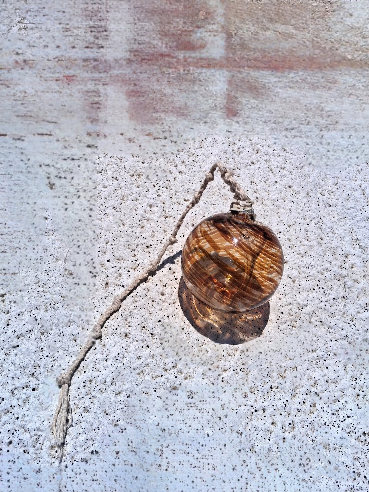 Close up of amber swirl handblown glass witch ball showing swirling honey and clear glass detail in sunlight