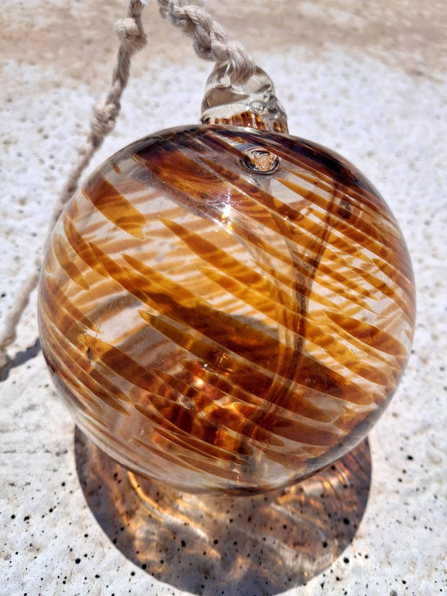 Amber witch ball close up showing handblown glass swirl texture and braided rope loop hanger detail