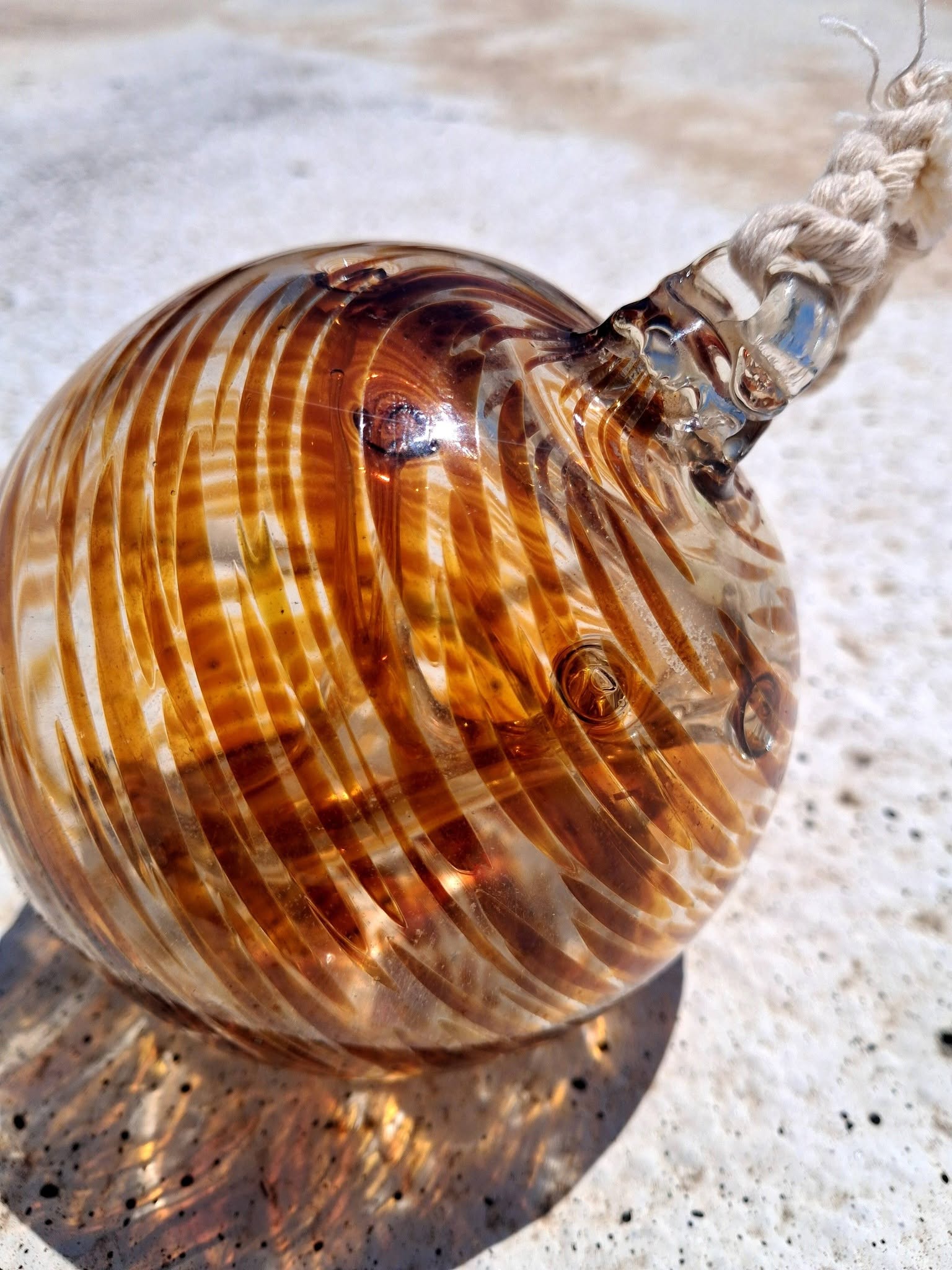 Top view of amber swirl witch ball showing braided rope hanger and glass loop attachment detail