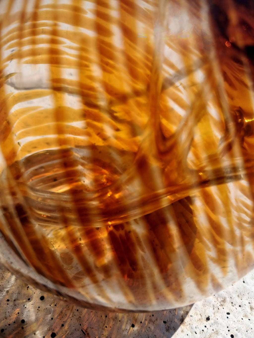 Amber handblown glass witch ball side view on concrete showing full round orb shape and rope hanger