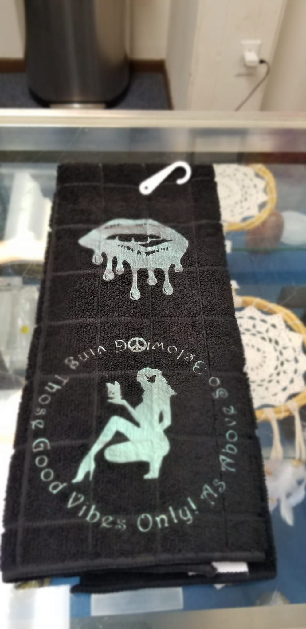 Black microfiber hand towel with teal dripping lips and Good Vibes Only As Above So Below seated woman silhouette handmade design in store display