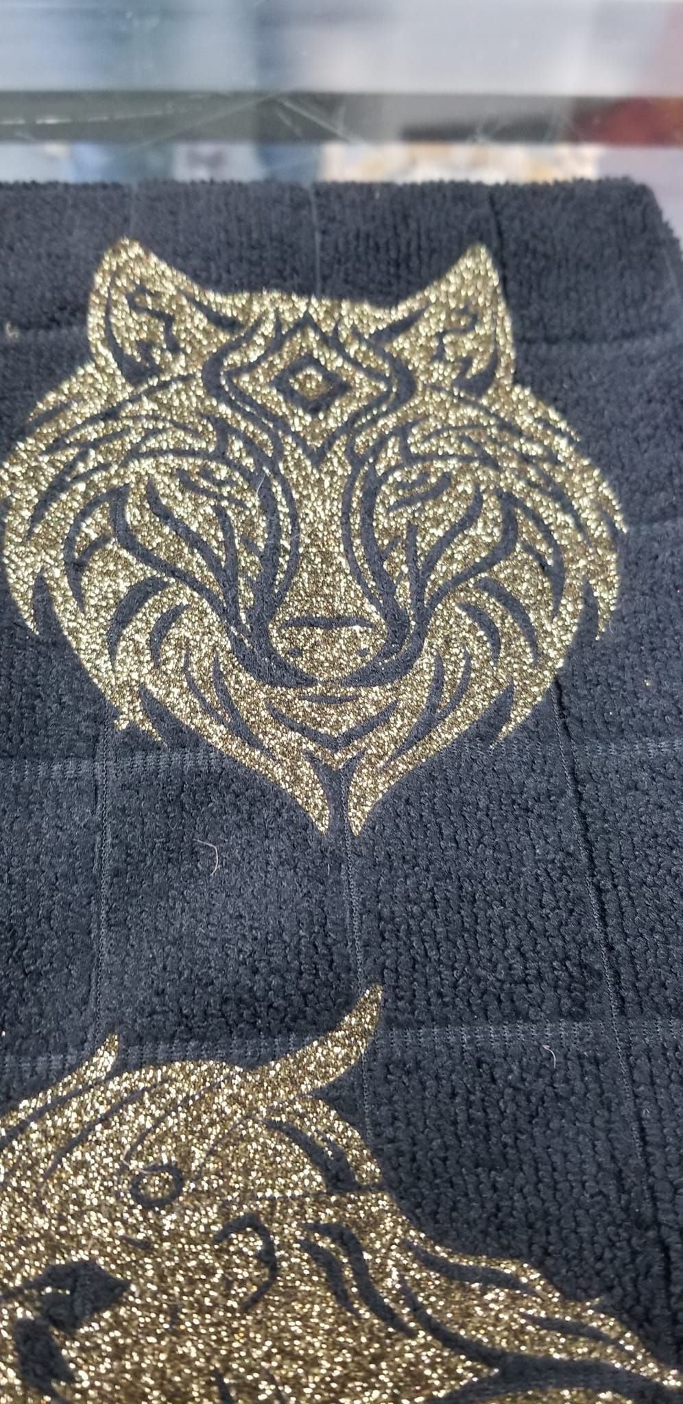 Close up of gold glitter tribal wolf face and Viking warrior design on black microfiber hand towel on pink surface