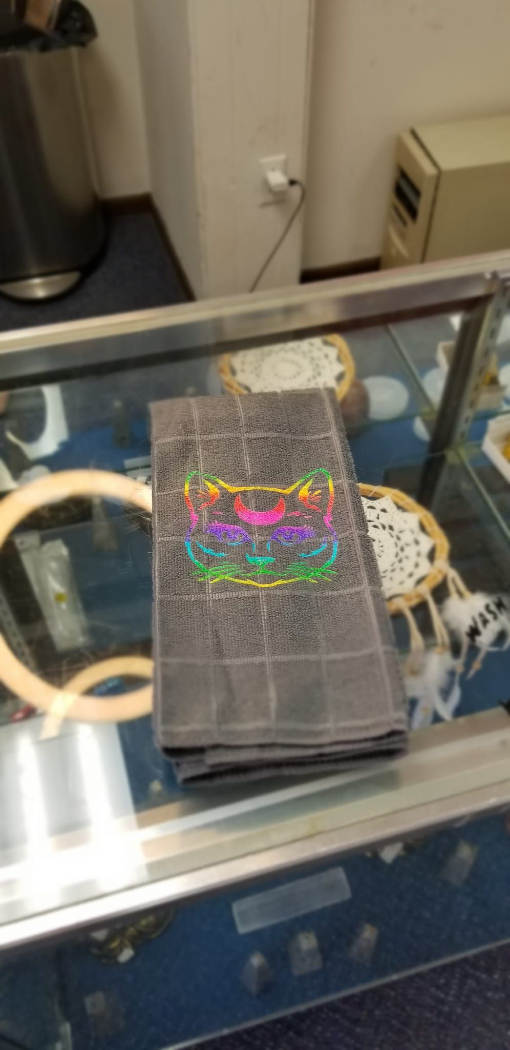 Rainbow moon cat hand towel full view in store display case showing mystical cat face with purple eyes
