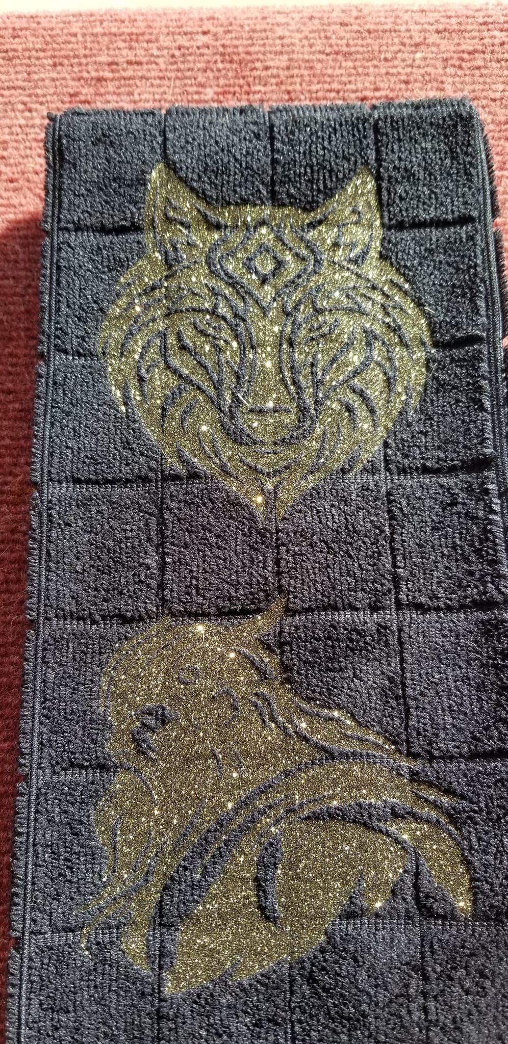 Black microfiber wolf and Viking warrior hand towel folded on concrete showing gold glitter design