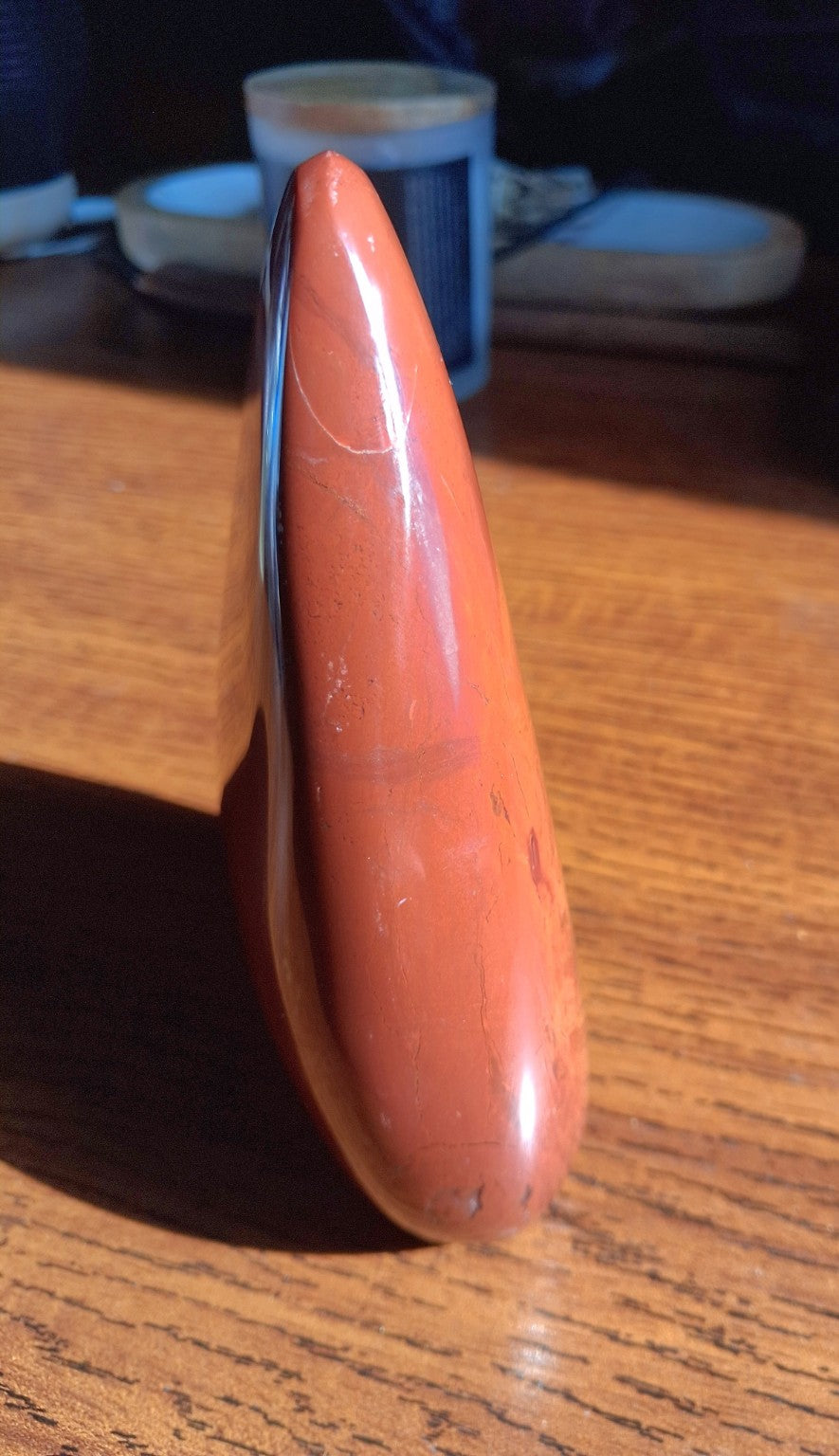 Red Jasper polished freeform slender side profile with glossy surface on wooden tabletop