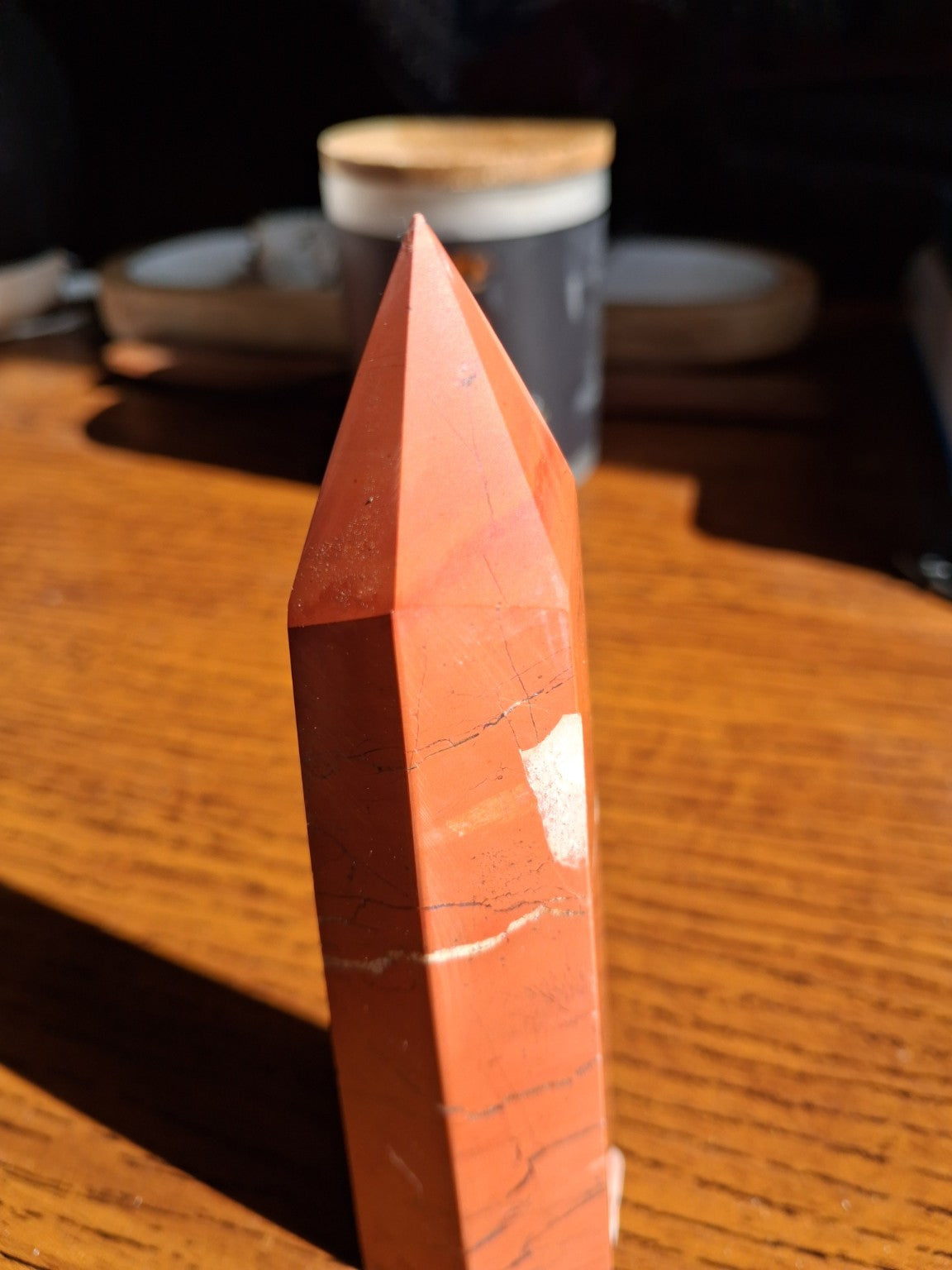 Original side view of natural red jasper stone faceted tower with thin charcoal veins and pale mineral patch