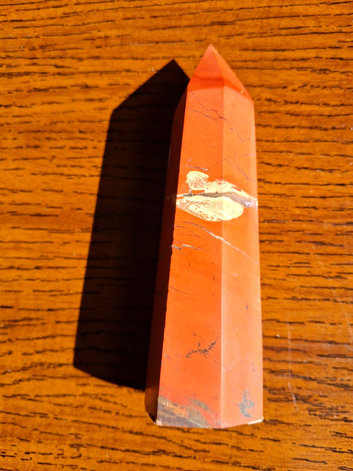 Original close photo of red jasper mineral point showing fine dark patterns, contrasting cream section and natural red color